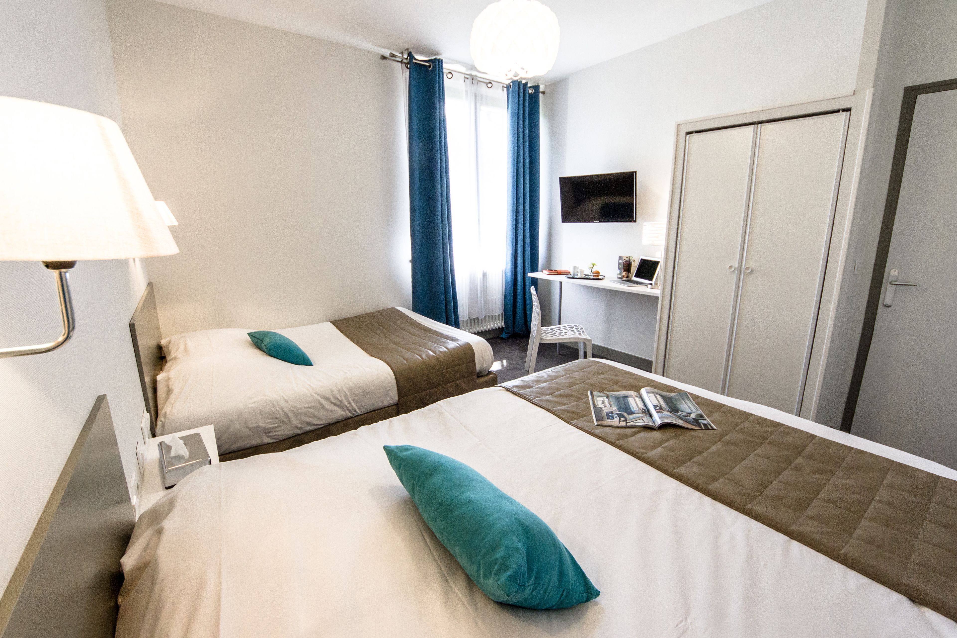 A hotel room with two beds, a desk with a computer, a TV, and a wardrobe.