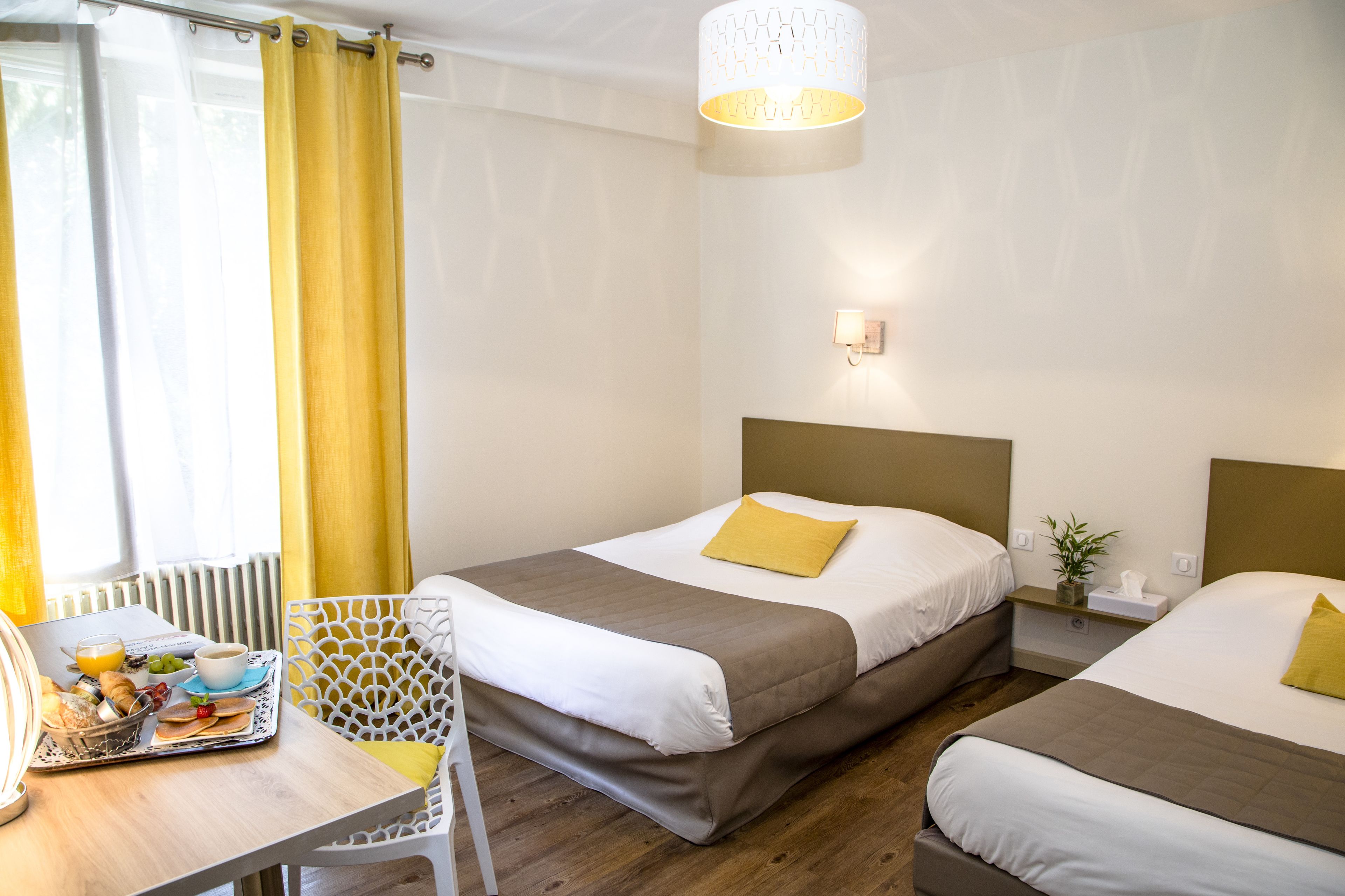 A hotel room with two beds, a breakfast tray, a table, and a window with curtains.