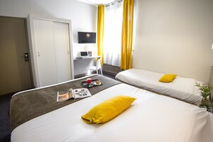 Quarto de hotel com duas camas, uma escrivaninha com computador, televisão e janela com cortinas amarelas.