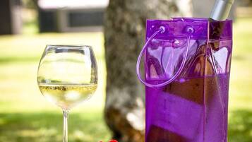 A glass of white wine, a purple bag, and some olives and cherry tomatoes on a table outdoors.