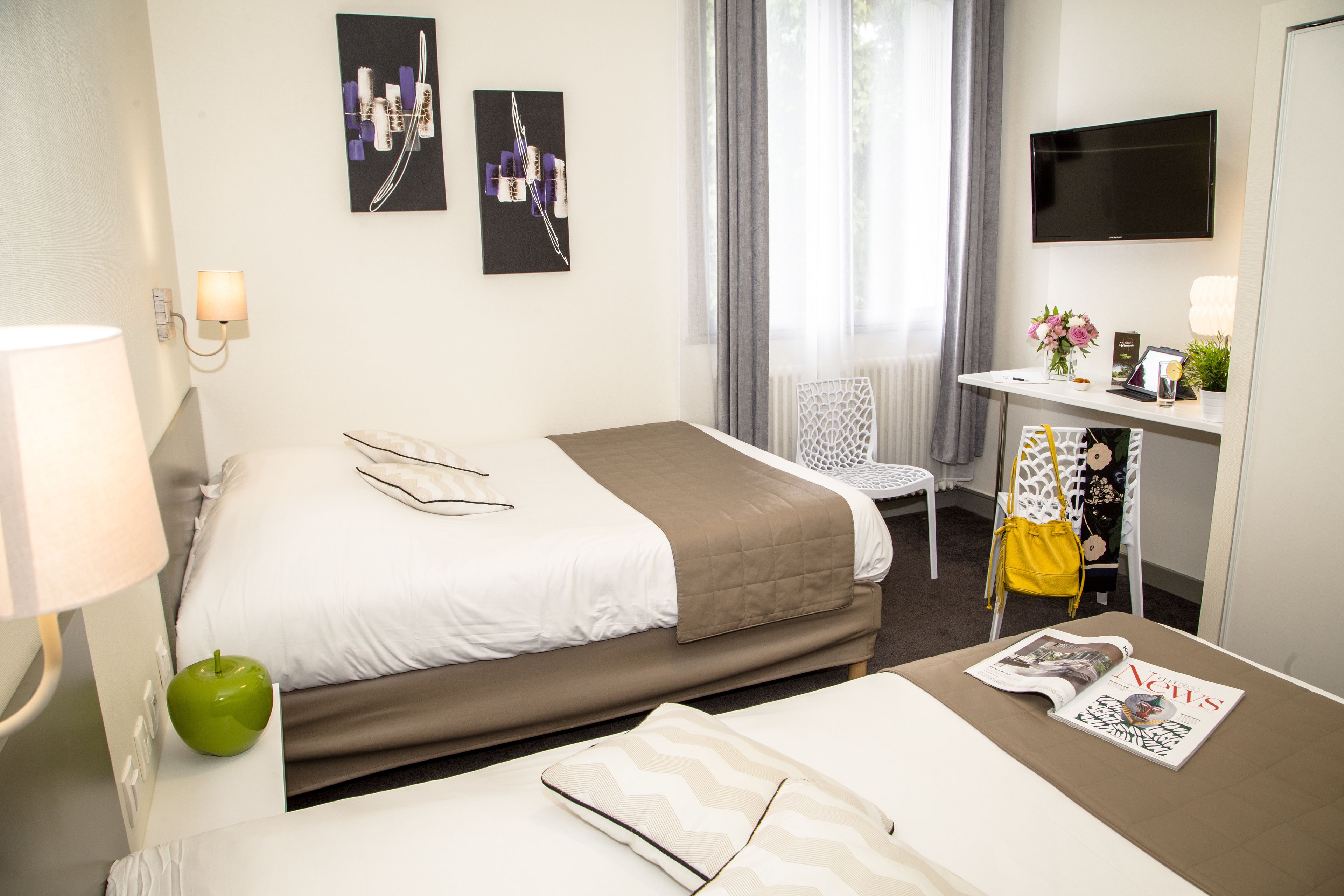 A hotel room with two beds, a desk with a TV, a lamp, and a magazine on the bed.
