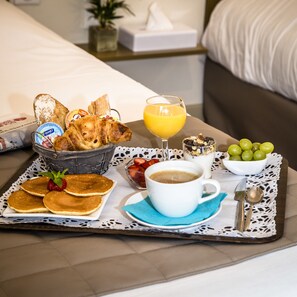 Un vassoio per la colazione con pancake, croissant, una ciotola di uva, un bicchiere di succo d'arancia e una tazza di caffè.