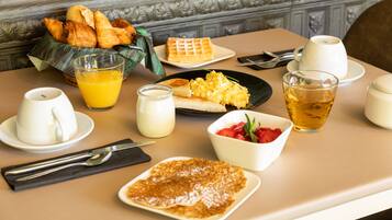 A breakfast table with croissants, waffles, scrambled eggs, toast, pancakes, a bowl of strawberries, a glass of orange juice, a glass of tea, and a cup of coffee.