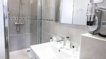 A modern bathroom with a glass-enclosed shower, a white vanity with a mirror, and a hairdryer mounted on the wall.