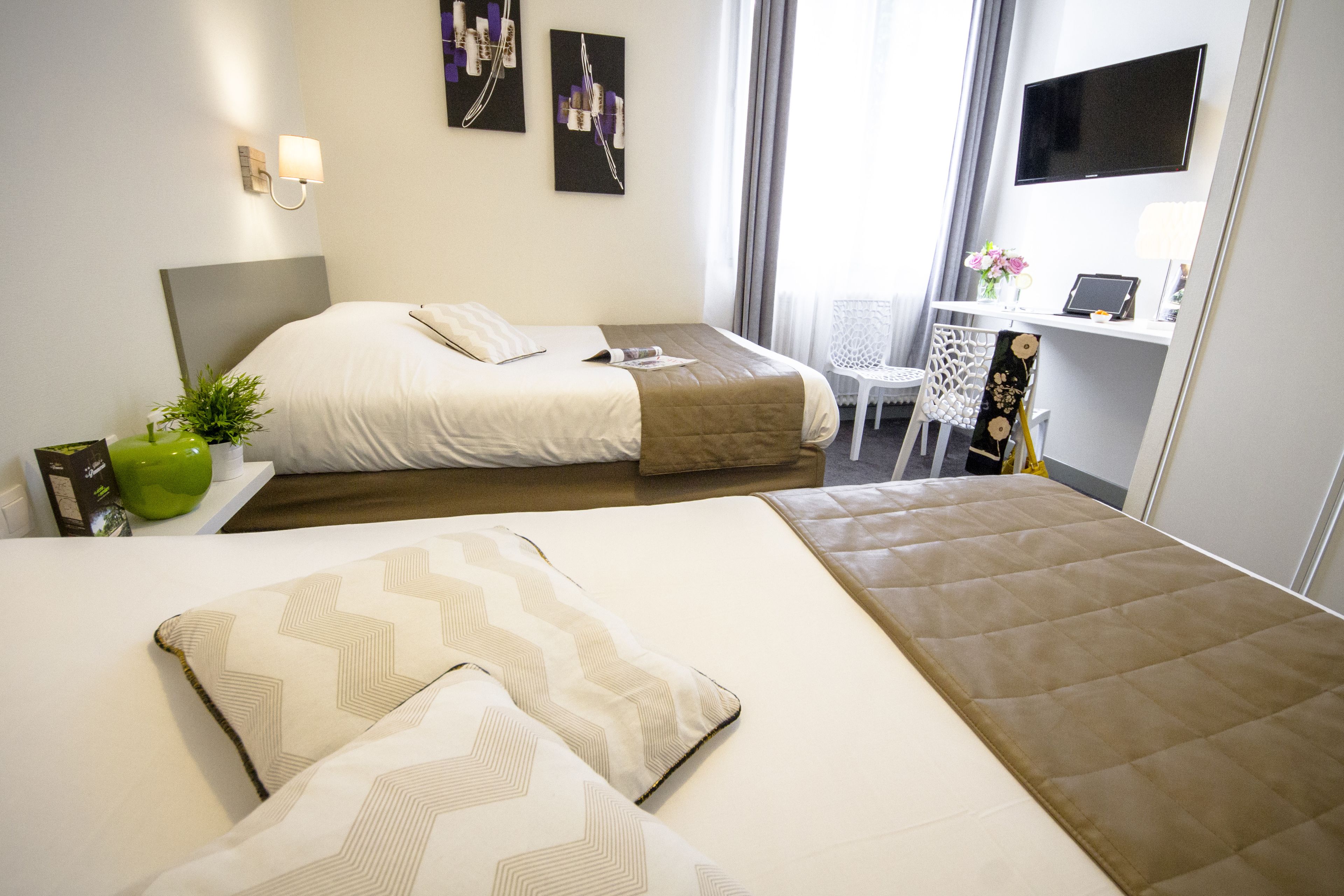 A hotel room with two beds, a desk, a TV, and artwork on the walls.