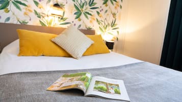 Una cama con almohadas amarillas y blancas, una revista sobre la cama, y un papel tapiz floral de fondo.