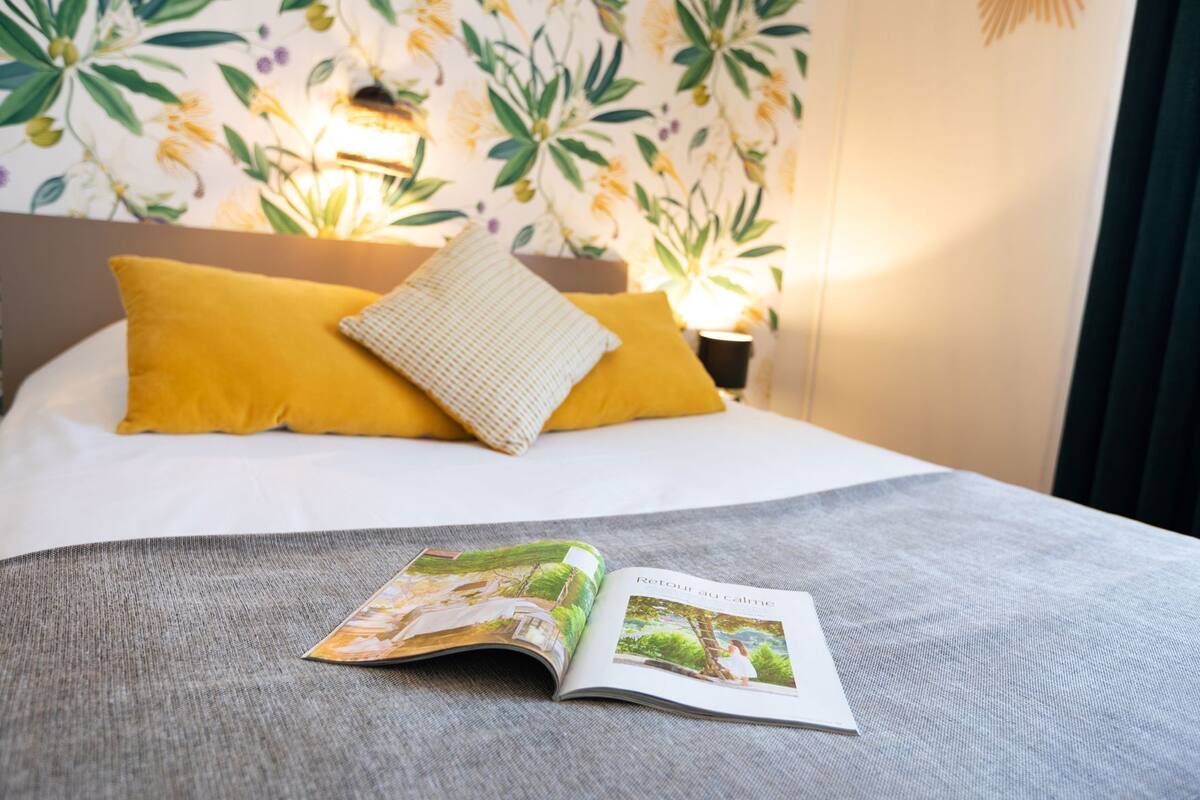 Un lit avec un magazine, un oreiller jaune et un papier peint à motifs.