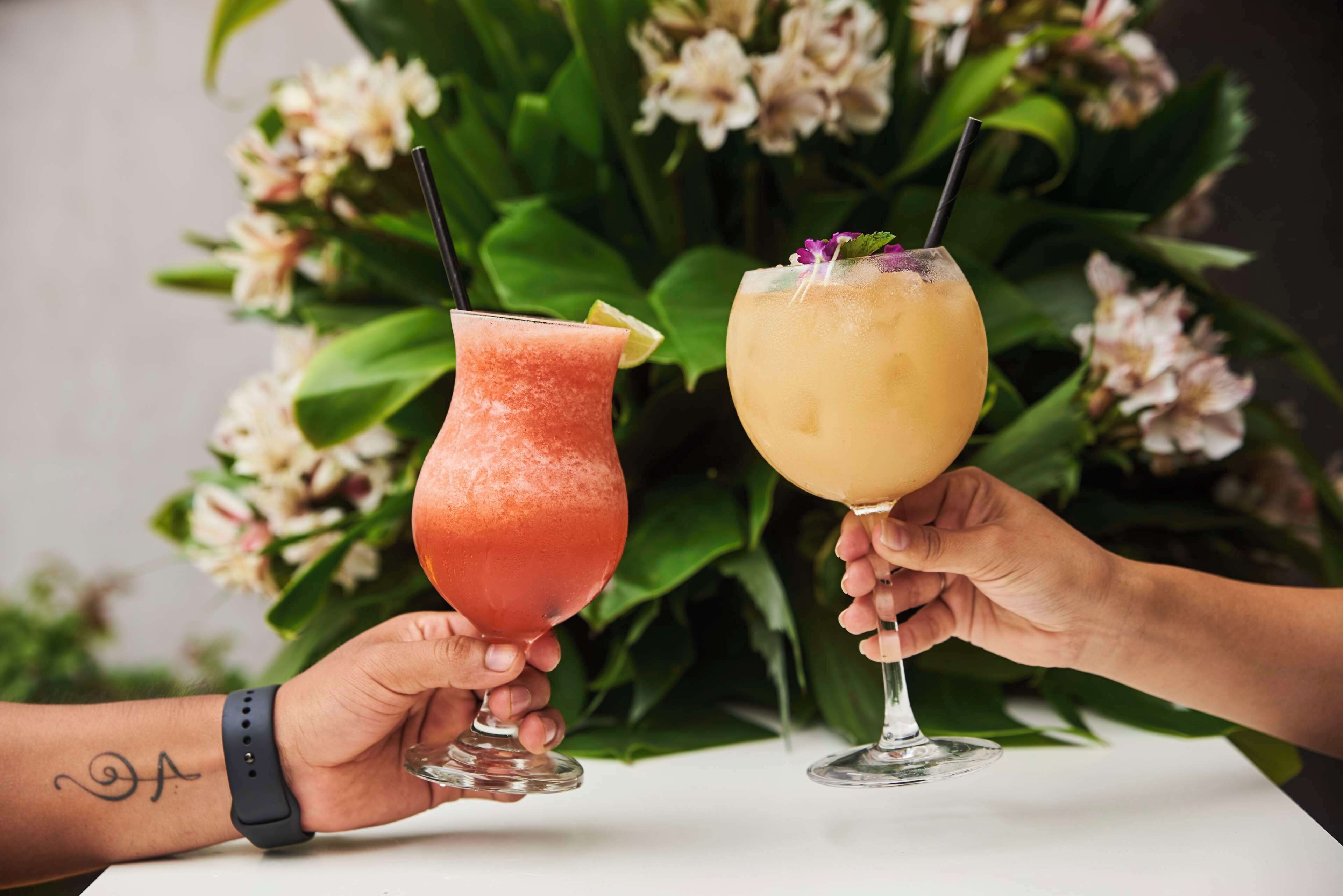 Two people holding cocktail glasses with a floral background.