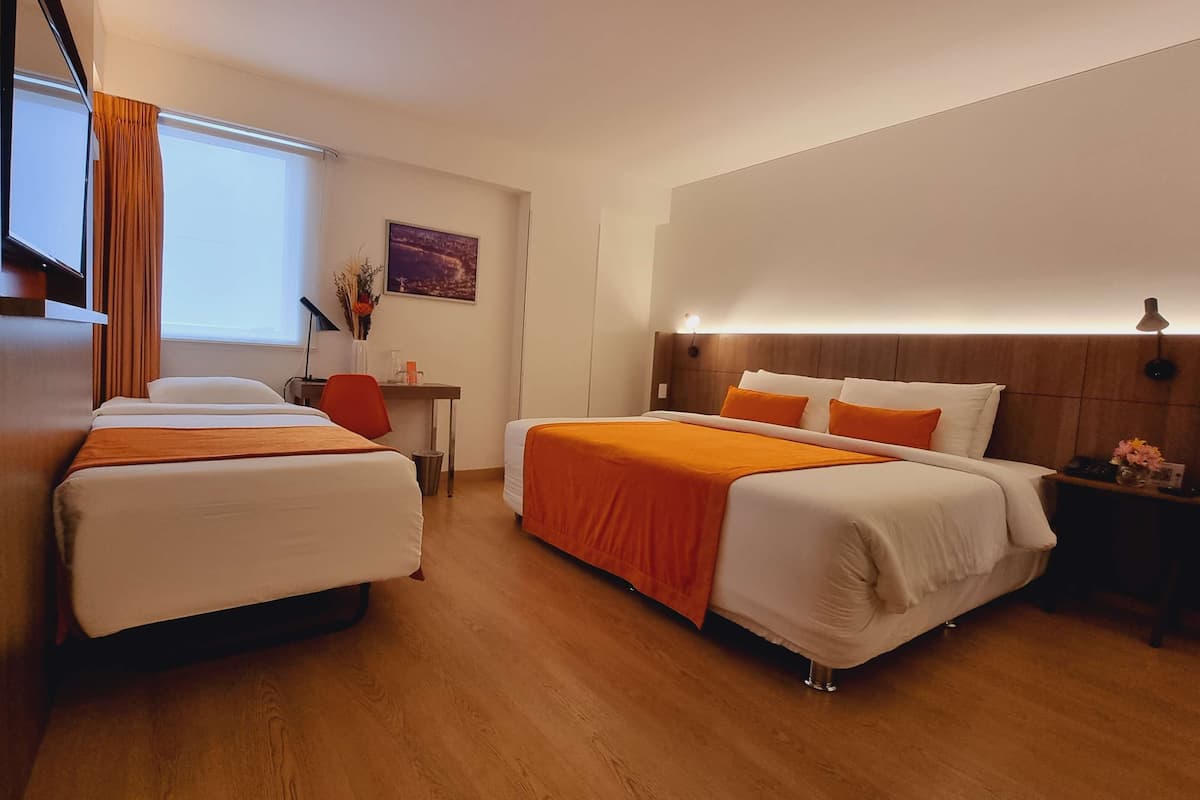 A hotel room with two beds, a wooden headboard, a nightstand, a desk, and a window with curtains.