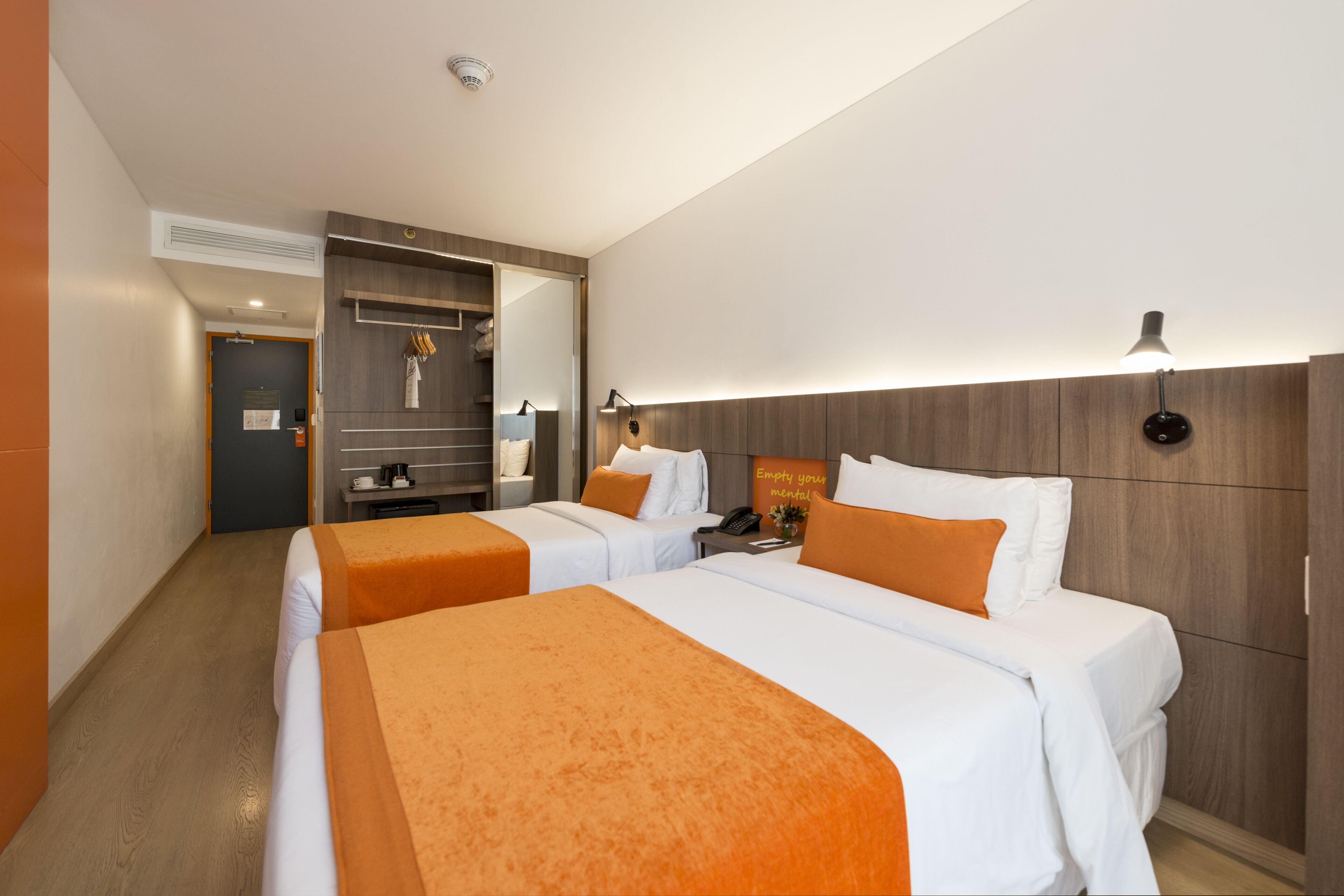 A hotel room with two beds, a wooden headboard, a desk, and a mirror.
