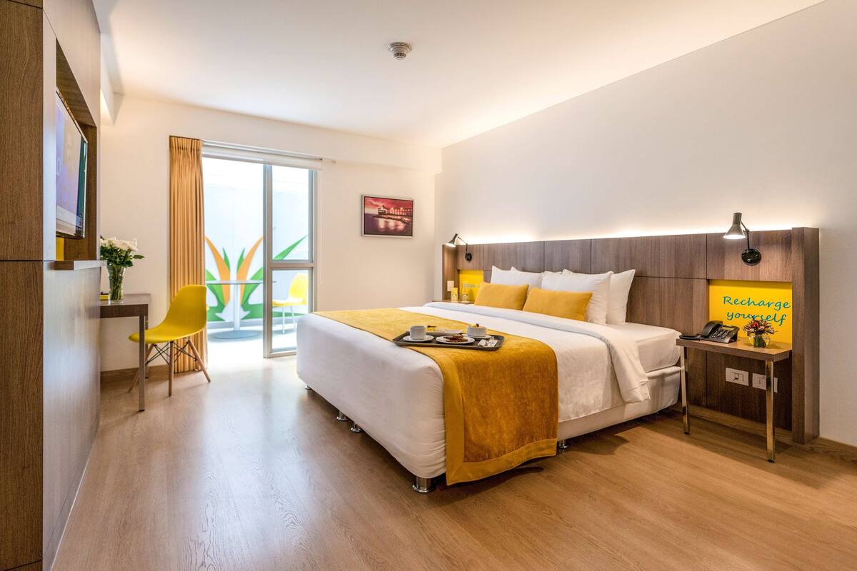 A hotel room with a bed, bedside table, chair, and a view of the outdoors.