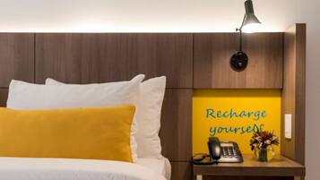 Een hotelkamer met een bed, een nachtkastje met een lamp, een telefoon en een bordje met de tekst