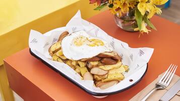 A tray of food with a fried egg and potatoes on a table with a vase of flowers.