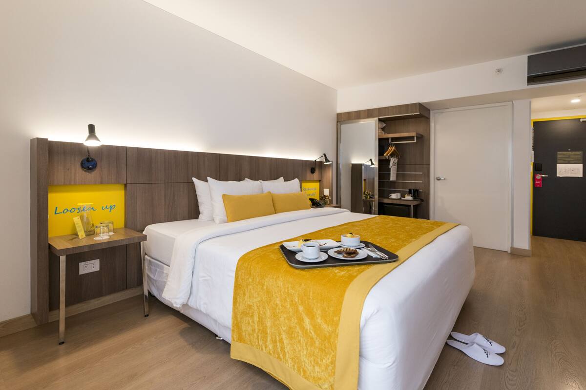 A hotel room with a bed, bedside table, and a tray with breakfast items.