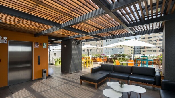 A modern indoor lounge with a wooden ceiling, a black sofa, and white tables. - Libre Hotel, BW Signature Collection (Lima)