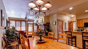 Zona pranzo con tavolo in legno, sedie e lampadario. C’è una pianta sul tavolo e una ventola a soffitto sullo sfondo.