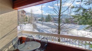 Un balcone con tavolo e sedie, affaccia su una via innevata con edifici e alberi.
