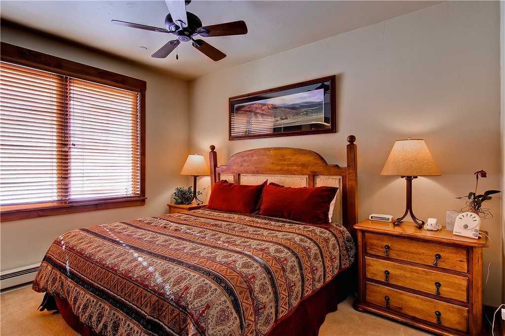 A bedroom with a bed, two bedside lamps, a nightstand, a ceiling fan, and a framed picture on the wall.