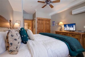 A bedroom with a bed, pillows, a ceiling fan, a TV, and a wooden wardrobe.