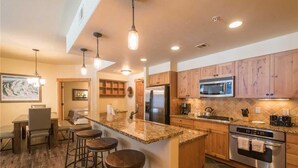 A kitchen with granite countertops, wooden cabinets, stainless steel appliances, and bar stools. - 4103 Aspen Lodge, Trappeur's Crossing (Condo) Apartment 3 (Steamboat Springs)