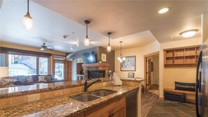 A spacious kitchen with granite countertops, a double sink, and a built-in dishwasher. There is a seating area with a sofa and a coffee table, and a large window providing natural light. - 4103 Aspen Lodge, Trappeur's Crossing (Condo) Apartment 3 (Steamboat Springs)