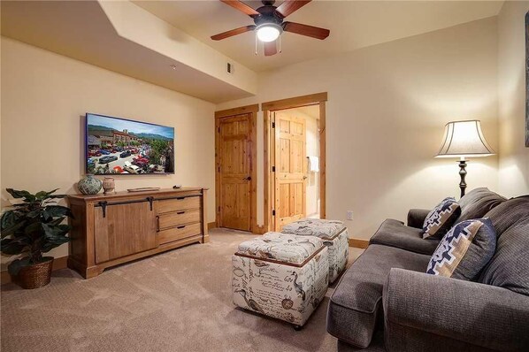 A living room with a sofa, ottoman, wooden cabinet, and a ceiling fan. - 4201 Aspen Lodge, Trappeur's Crossing Apartment 3 (Steamboat Springs)