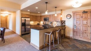 A modern kitchen with wooden cabinets, stainless steel appliances, a central island with bar stools, pendant lighting, and a clock on the wall. - 4201 Aspen Lodge, Trappeur's Crossing Apartment 3 (Steamboat Springs)