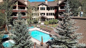 A resort with a swimming pool surrounded by lounge chairs and a large building with multiple balconies. - 4201 Aspen Lodge, Trappeur's Crossing Apartment 3 (Steamboat Springs)