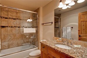 A bathroom with a glass-enclosed shower, a bathtub, a sink with a granite countertop, and a large mirror.