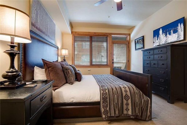 A bedroom with a bed, bedside lamps, a dresser, and a window with blinds.