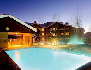 A hotel with a swimming pool, a covered entrance, and a ski lift visible in the background.