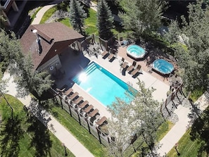 An aerial view of a residential property with a swimming pool, hot tub, and outdoor seating area surrounded by trees.