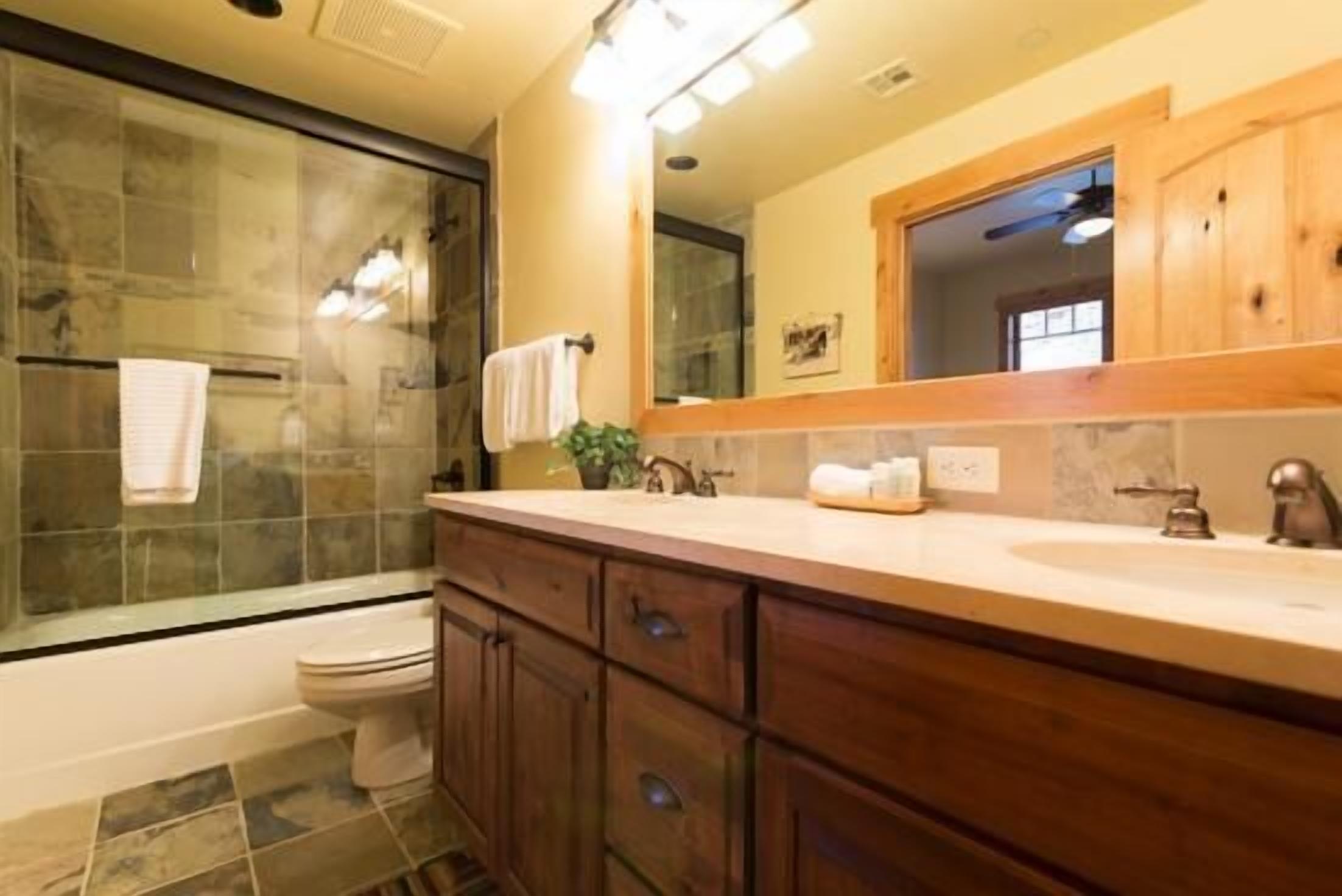 A bathroom with a glass shower enclosure, a white toilet, wooden cabinets, and a large mirror above the sink.