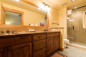 A modern bathroom with a wooden vanity, a large mirror, a glass shower enclosure, and a toilet.