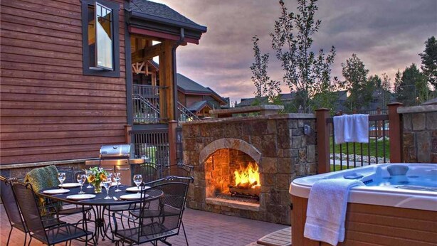 A patio with a stone fireplace, a hot tub, and a dining table set for four. - 6106 Bear Lodge, Trappeur's Crossing Apartment 5 (Steamboat Springs)