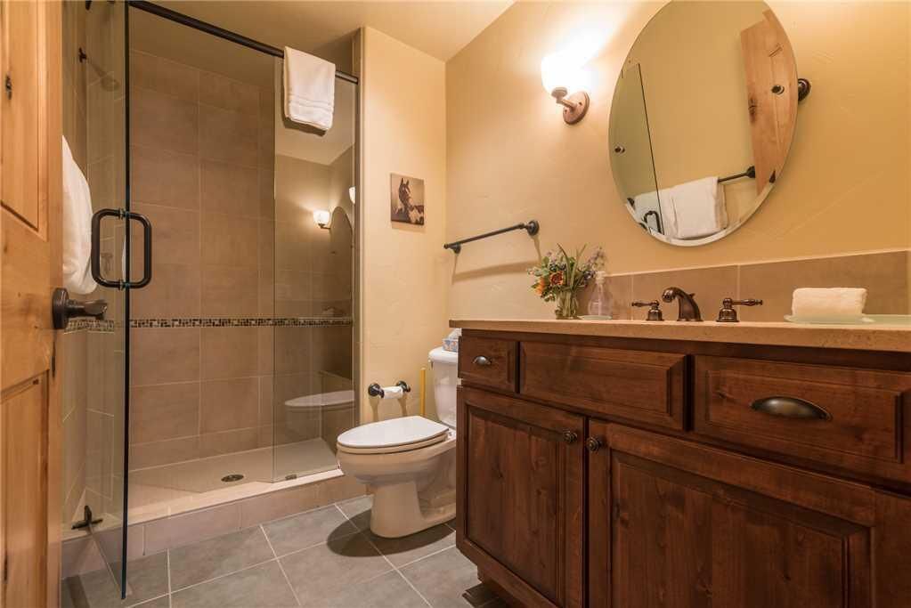 Een badkamer met een douchecabine van glas, een toilet, een houten wastafelmeubel met lades en een ronde spiegel.