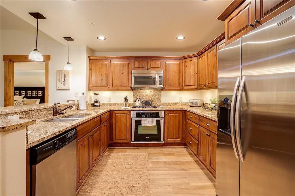 A kitchen with wooden cabinets, stainless steel appliances, granite countertops, and pendant lighting.