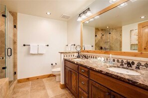 Une salle de bain dotée d’une douche à parois de verre, d’un meuble-lavabo en bois avec un plan de travail en marbre et d’un grand miroir au-dessus du lavabo.