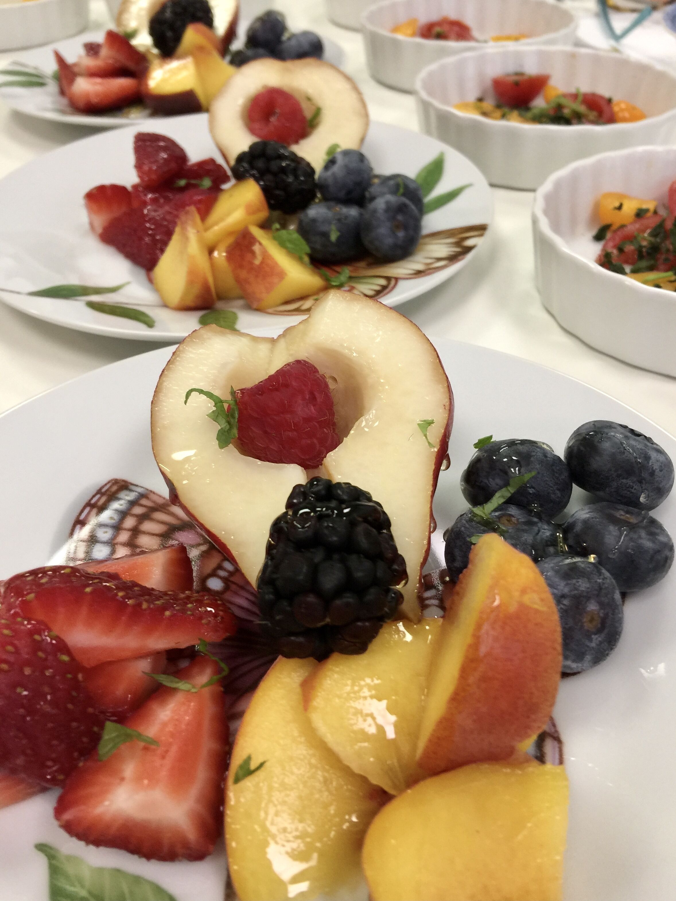 A variety of fruit arranged on plates, including strawberries, blackberries, blueberries, and peaches.