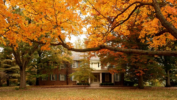 A two-story house with a front porch, surrounded by trees with autumn leaves. - Charred Oaks Inn (Versailles)