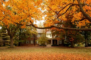A two-story house with a front porch, surrounded by trees with autumn leaves.