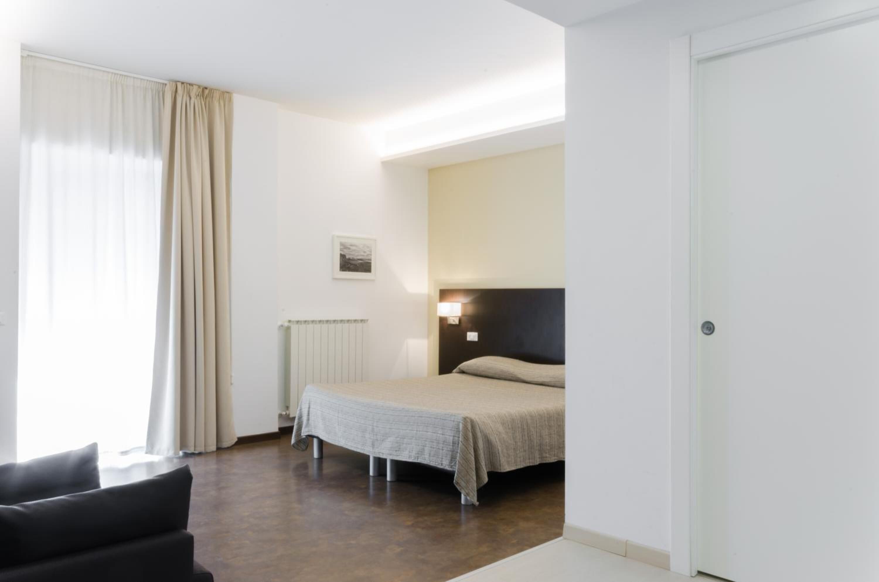 Una habitación de hotel con una cama, una silla, un radiador y una lámpara fijada a la pared.