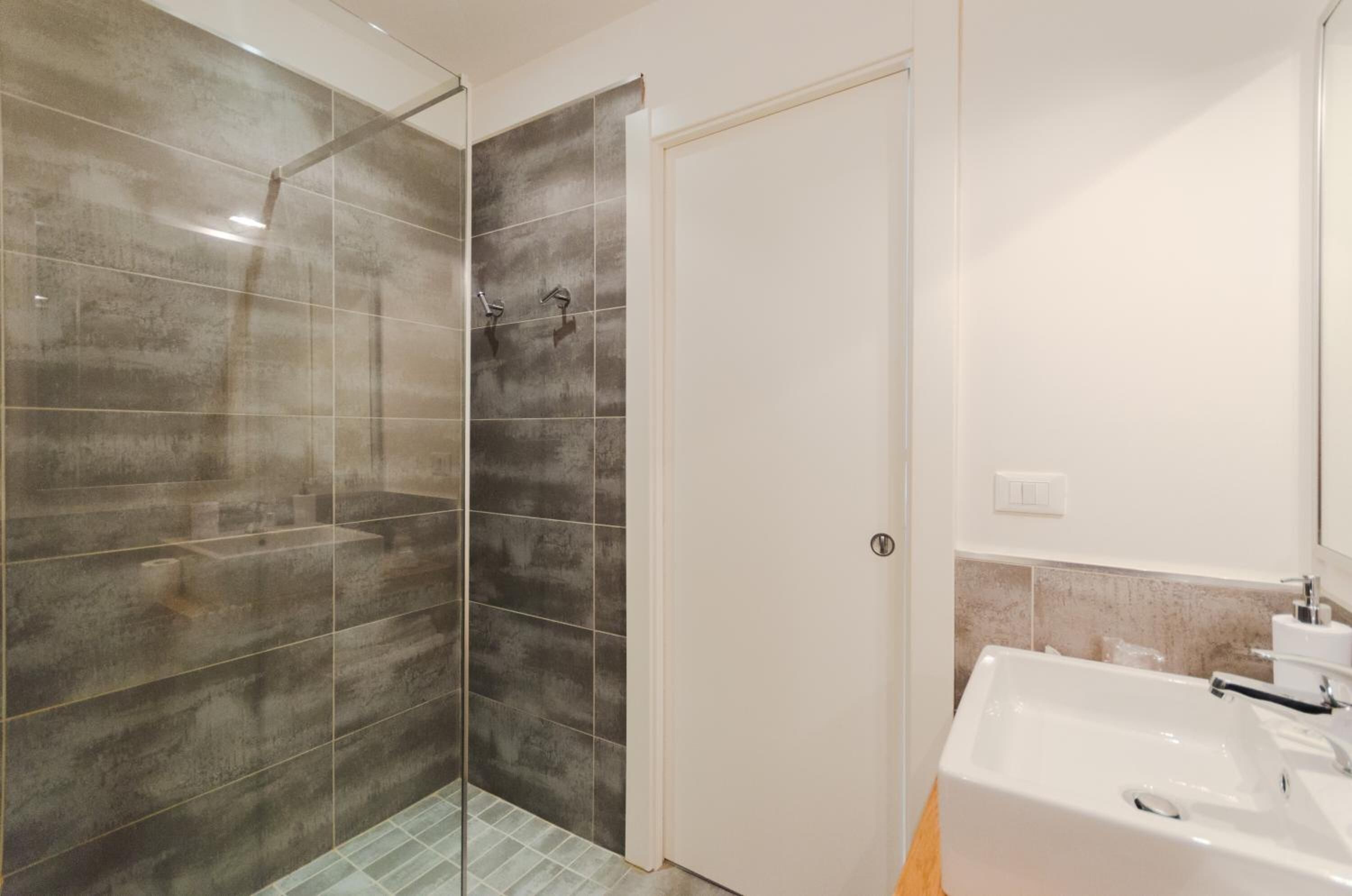 Un baño con cabina de ducha de vidrio, un lavamanos blanco y una puerta.