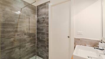 Un baño con cabina de ducha de vidrio, un lavamanos blanco y una puerta.