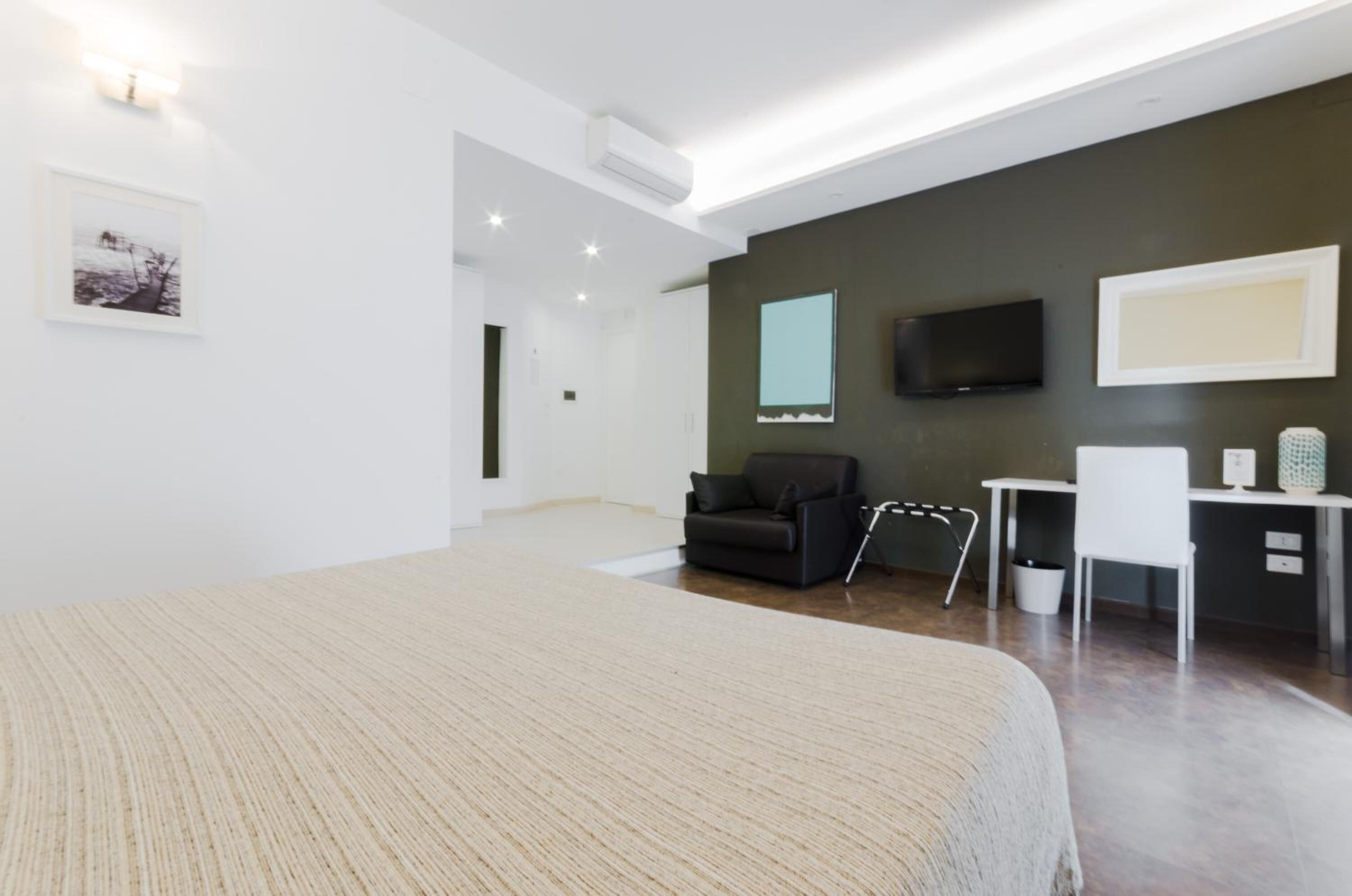 Una habitación de hotel moderna con una cama grande, un escritorio, una silla, un televisor y un cuadro en la pared.