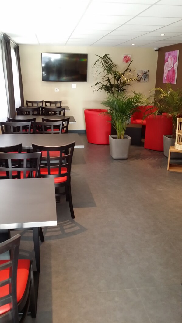 A modern indoor space with tables and chairs, a large flat-screen TV, and decorative plants.