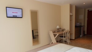 Une chambre d’hôtel équipée d’un lit, d’un bureau, d’une chaise, d’un miroir et d’un téléviseur affichant le mot « BIENVENUE ».