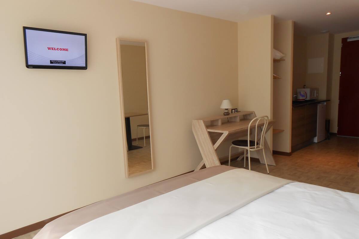 Ein Hotelzimmer mit Bett, Schreibtisch, Stuhl, Spiegel und Fernseher, der "WELCOME" anzeigt.