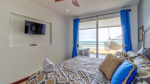 Een slaapkamer met een bed, een aan de muur bevestigde televisie en een balkon met uitzicht op de oceaan.