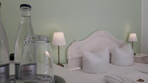 A neatly made bed with white linens and pillows, a bedside table with a lamp, and a bottle of water on the nightstand. - Erbenholz Hotel (Laatzen)